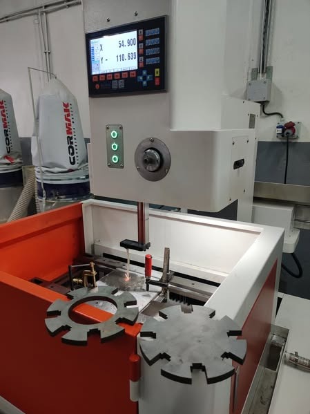 Elektroerozyjna obróbka metali: detale zębate na stole roboczym maszyny. Widoczny panel sterowania i iskra podczas procesu obróbki. Elementy mocujące w tle.