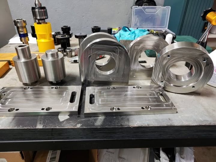 Precyzyjnie obrobione metalowe elementy z widocznymi śladami frezowania, leżące na warsztatowym stole w otoczeniu narzędzi i akcesoriów.