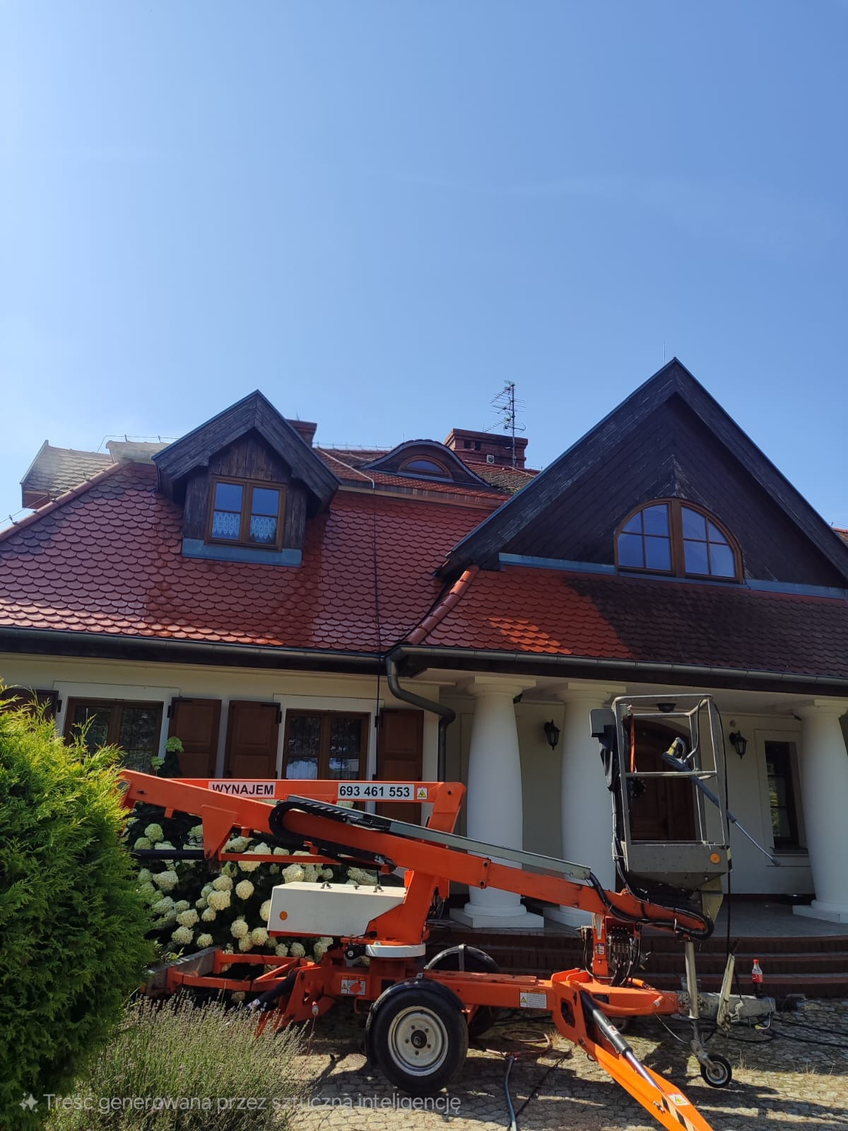 Praca na wysokościach: pomarańczowy podnośnik koszowy przed domem z czerwoną dachówką i białymi kolumnami. Usługi wysokościowe.