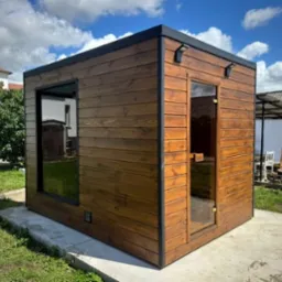 Nowoczesna sauna ogrodowa z drewna w Andrychowie. Widoczna przeszklona ściana i drzwi, oświetlenie zewnętrzne. Całość na betonowej wylewce.