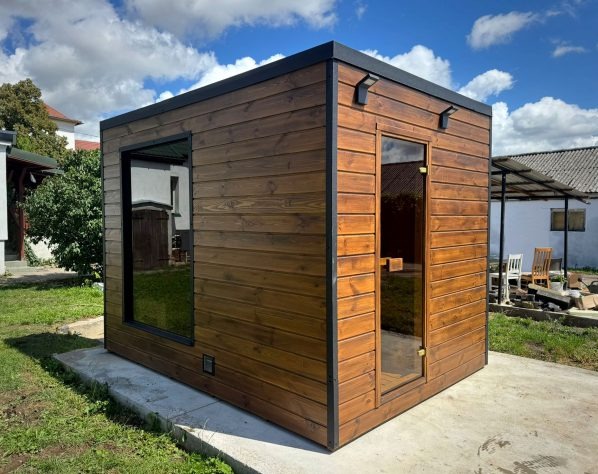 Nowoczesna sauna ogrodowa z drewna w Andrychowie. Widoczna przeszklona ściana i drzwi, oświetlenie zewnętrzne. Całość na betonowej wylewce.