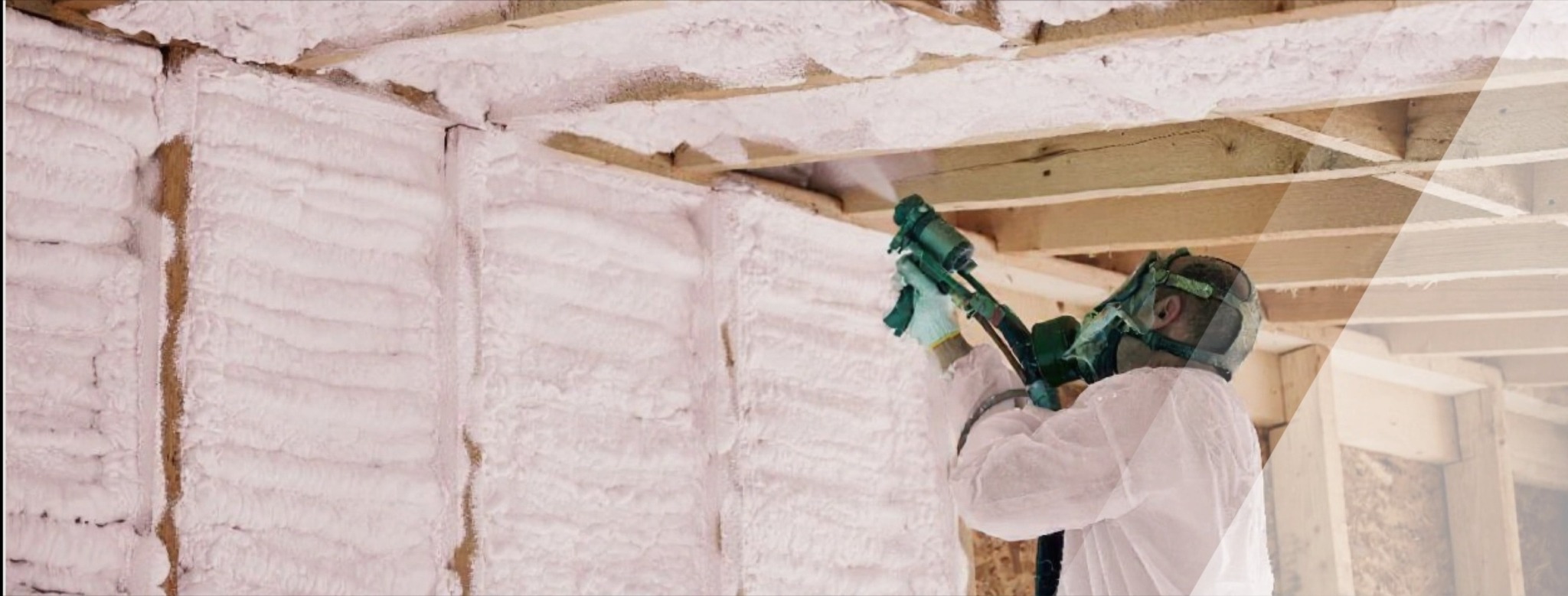 Pracownik w kombinezonie nanosi piankę PUR na ściany i sufit poddasza, tworząc warstwę izolacyjną. Widoczne drewniane belki i świeża, biała pianka.