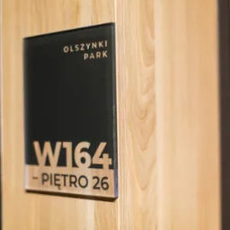 Oznakowanie biura: tabliczka z nazwą 'Olszynki Park', numerem W164 i informacją o piętrze 26, zamocowana na drewnianej ścianie.