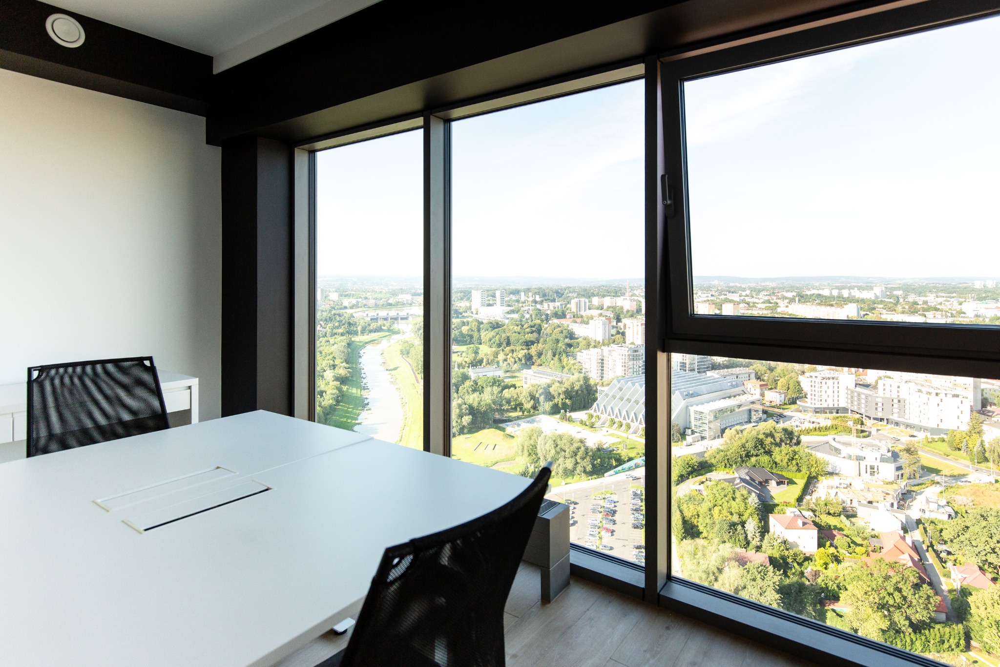 Jasne biuro z dużym oknem i widokiem na panoramę miasta. Biały stół konferencyjny i krzesła. Nowoczesne wnętrze w minimalistycznym stylu.