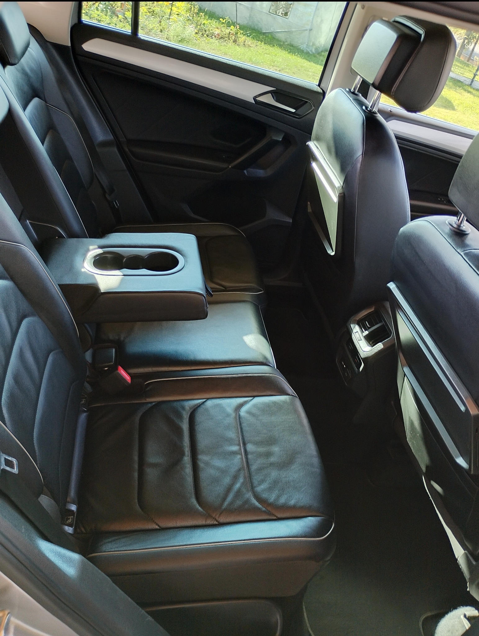 Wnętrze samochodu z czarną skórzaną tapicerką, widok na tylne siedzenia z rozkładanym podłokietnikiem i uchwytami na napoje. Widoczne detale wykończenia wnętrza.