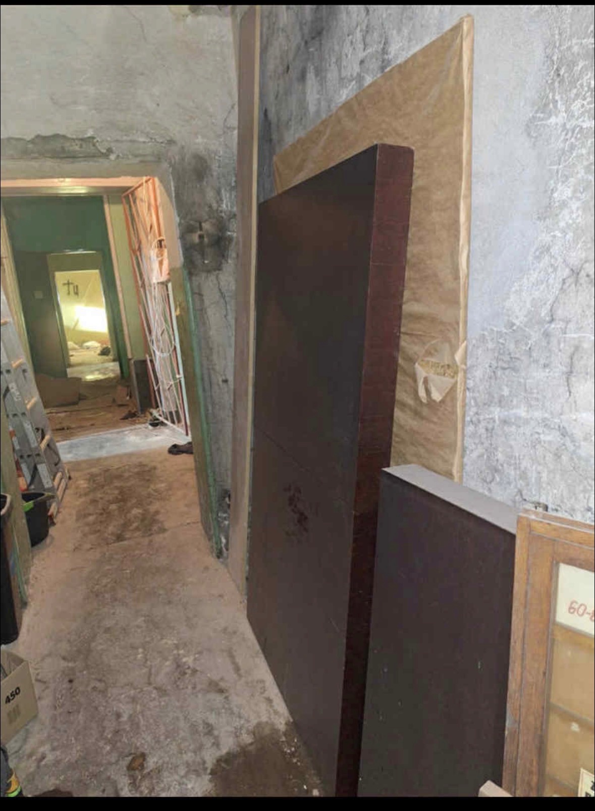 Korytarz w piwnicy z meblami przygotowanymi do wyniesienia. Widoczne schody, ściany z odrapanym tynkiem i kartony. Przygotowanie do transportu.