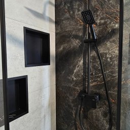 Glądys usługi remontowo budowlane - Nowoczesna łazienka z czarną armaturą i wnękami w ścianie wyłożonej szarymi i marmurkowymi płytkami. Minimalistyczny design, eleganckie wykończenie.