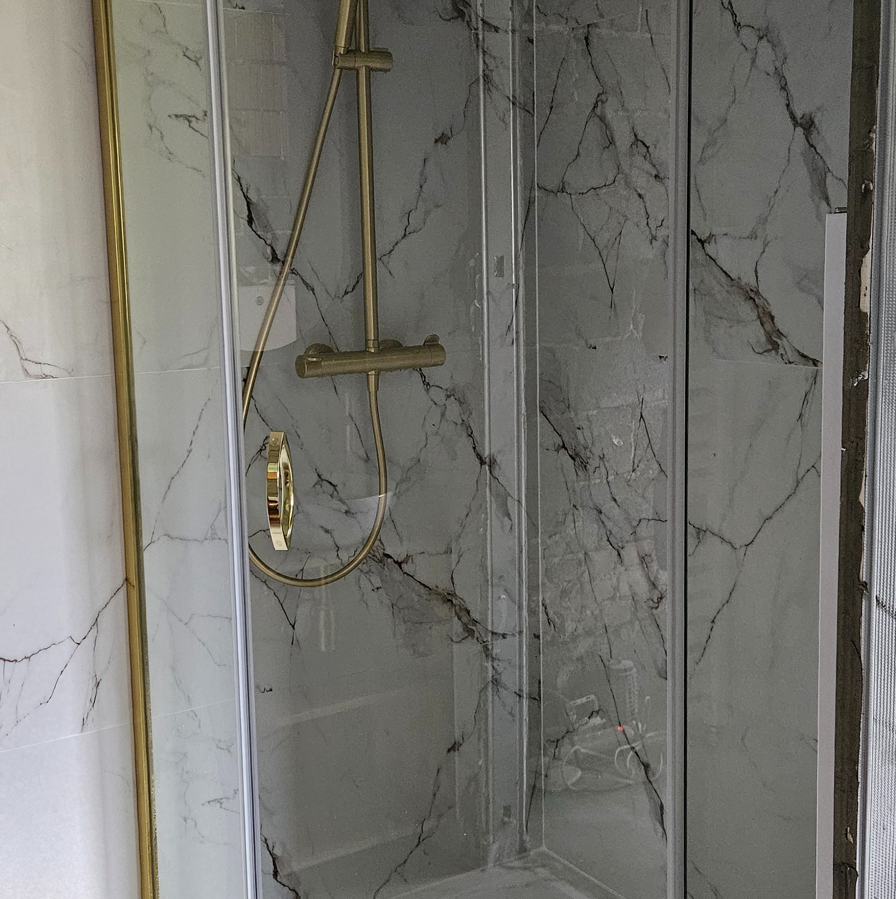 Kabina prysznicowa z armaturą w kolorze złota i marmurowymi płytkami, widok z bliska na wykończoną łazienkę. Elementy wykończeniowe w trakcie montażu.