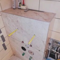 Obudowa stelaża WC z płytek imitujących marmur, z widocznymi przyłączami wodno-kanalizacyjnymi. Poziomica, młotek i szpachelka na górze. Detal wykończenia łazienki.