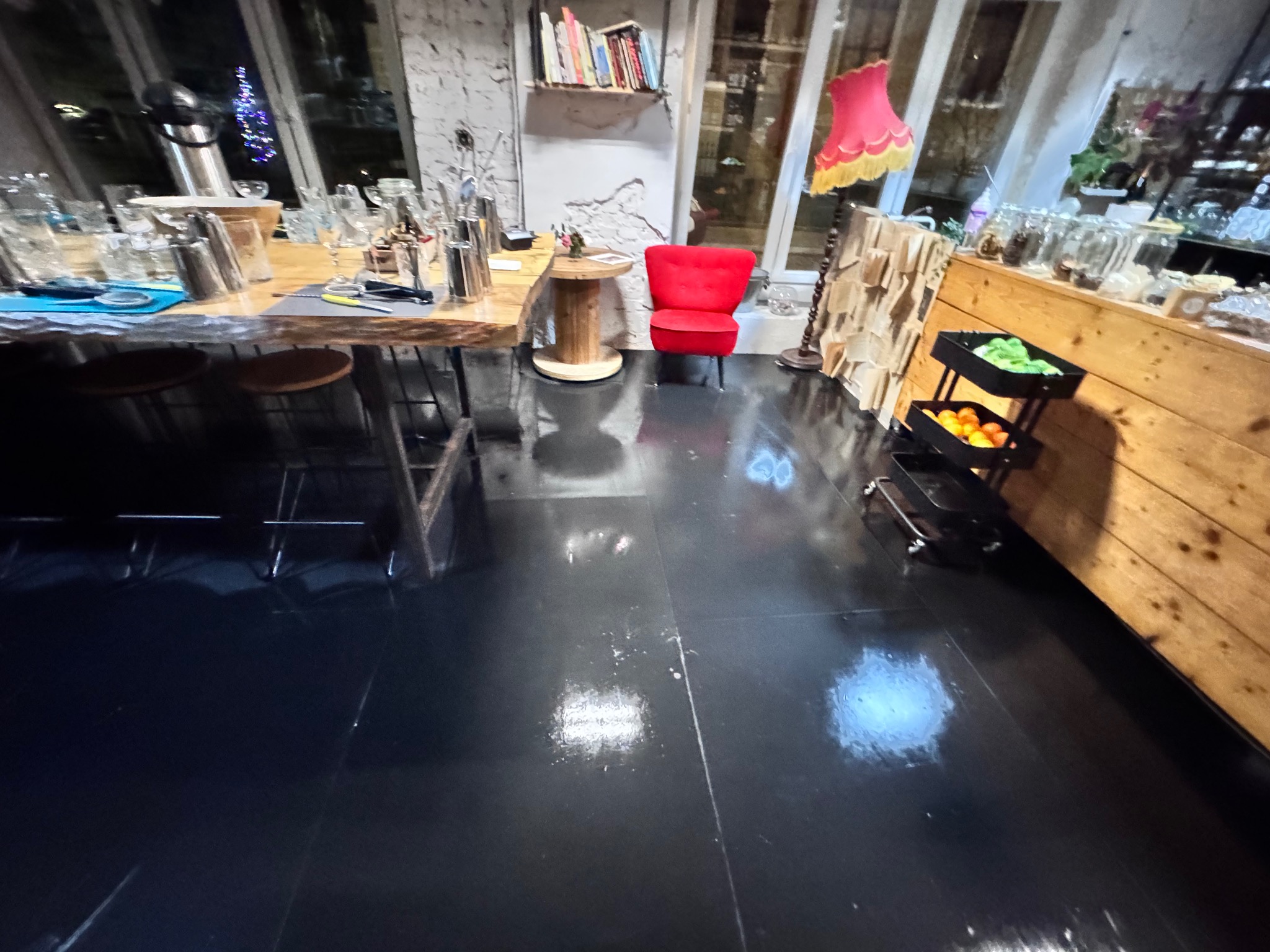 Błyszcząca, czarna podłoga po umyciu w lokalu w Gdańsku. Widoczny bar z akcesoriami, krzesła i dekoracje. Czystość i połysk podkreślają profesjonalizm.