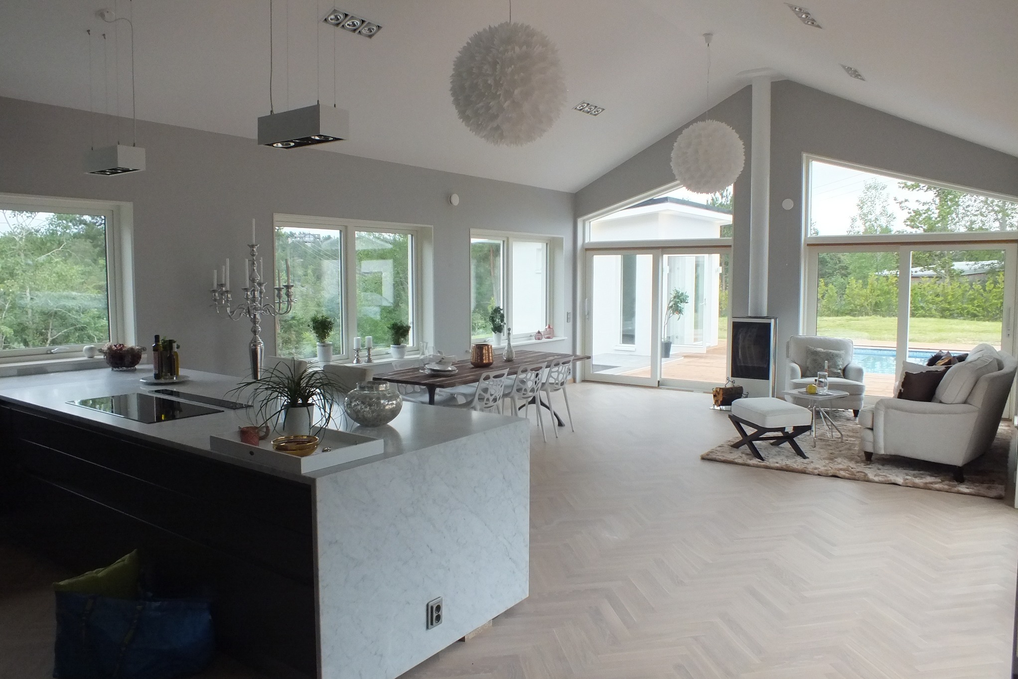 Jasne, przestronne wnętrze domu z parkietem w jodełkę, wyspą kuchenną z marmurowym wykończeniem i widokiem na basen przez duże okna.