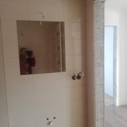 Robert Jaworski - Łazienka w trakcie remontu: jasne płytki, lustro z odbiciem osoby robiącej zdjęcie, widoczne przewody i otwory na armaturę. Surowy stan wykończenia.