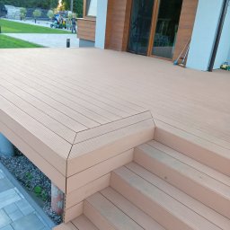 Robert Jaworski - Nowy taras z kompozytu, ze schodami, w odcieniach brązu, przylegający do nowoczesnego domu z dużymi oknami. Widok na zadbany trawnik i bawiące się dzieci.