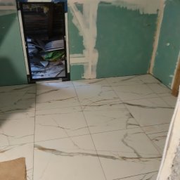 Robert Jaworski - Białe płytki podłogowe z marmurowym wzorem w pokoju na poddaszu, ściany w trakcie przygotowania do malowania, widoczne płyty gipsowe i szpachlowanie.