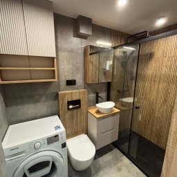 Robert Jaworski - Nowoczesna łazienka z kabiną prysznicową typu walk-in, umywalką nablatową, pralką Samsung i drewnianymi akcentami na ścianach i szafkach. Szaro-beżowa kolorystyka.