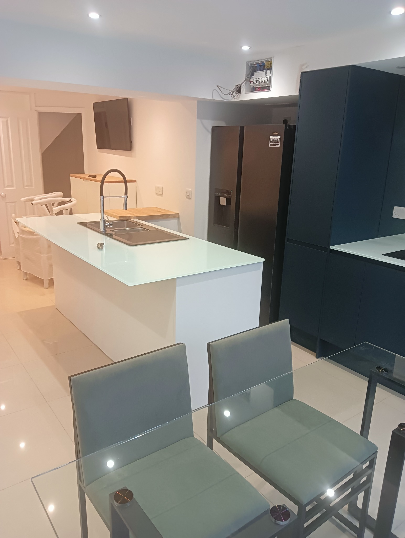 Nowoczesna kuchnia w Małym Miłobądzu z wyspą i ciemnymi szafkami. Widoczne szklane krzesła i stół. Minimalistyczny design, jasne płytki podłogowe.