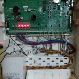 Otwarta obudowa centrali alarmowej Satel Integra 64 z widoczną elektroniką, licznymi przewodami i transformatorem. Zapalone diody sygnalizacyjne.