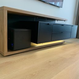 HYPER MEBLE Piotr Burdek - Nowoczesna szafka RTV na wymiar z oświetleniem LED, wykonana z drewna i czarnych frontów, z widocznym komputerem w przestrzeni otwartej.