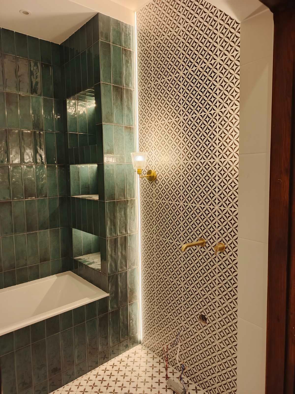Wykończona łazienka: zielone, połyskliwe płytki ścienne z wnękami, wzorzysta ściana, złota armatura, oświetlenie LED i podłoga w geometryczny wzór.