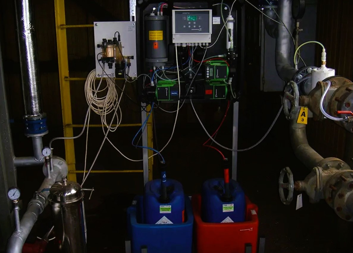Kompleksowy system uzdatniania wody z rurami, zbiornikami i panelami sterowania. Widoczne pompy dozujące w kolorowych pojemnikach.