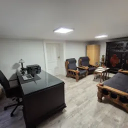 Eleganckie biuro w Łodzi z ciemnym biurkiem, laptopem i krzesłem biurowym. W tle antyczne meble i lampa. Stonowana kolorystyka, nowoczesne oświetlenie.