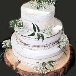 ZŁOTY KLUCZ SPÓŁKA Z OGRANICZONĄ ODPOWIEDZIALNOŚCIĄ - Trzypiętrowy tort weselny w stylu rustykalnym, z kremem typu naked cake i dekoracją z gipsówki, umieszczony na drewnianym plastrze pnia.