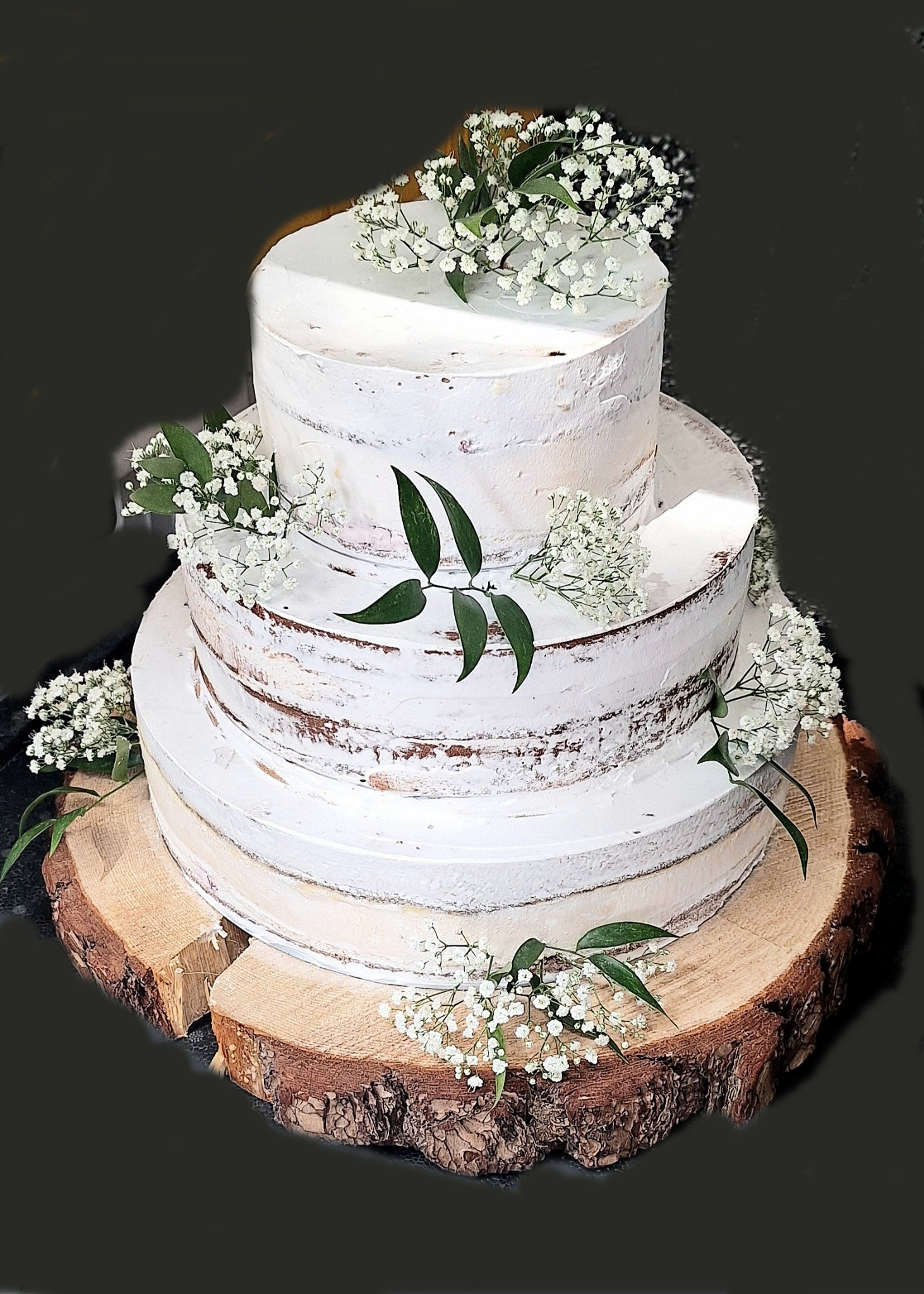Trzypiętrowy tort weselny w stylu rustykalnym, z kremem typu naked cake i dekoracją z gipsówki, umieszczony na drewnianym plastrze pnia.