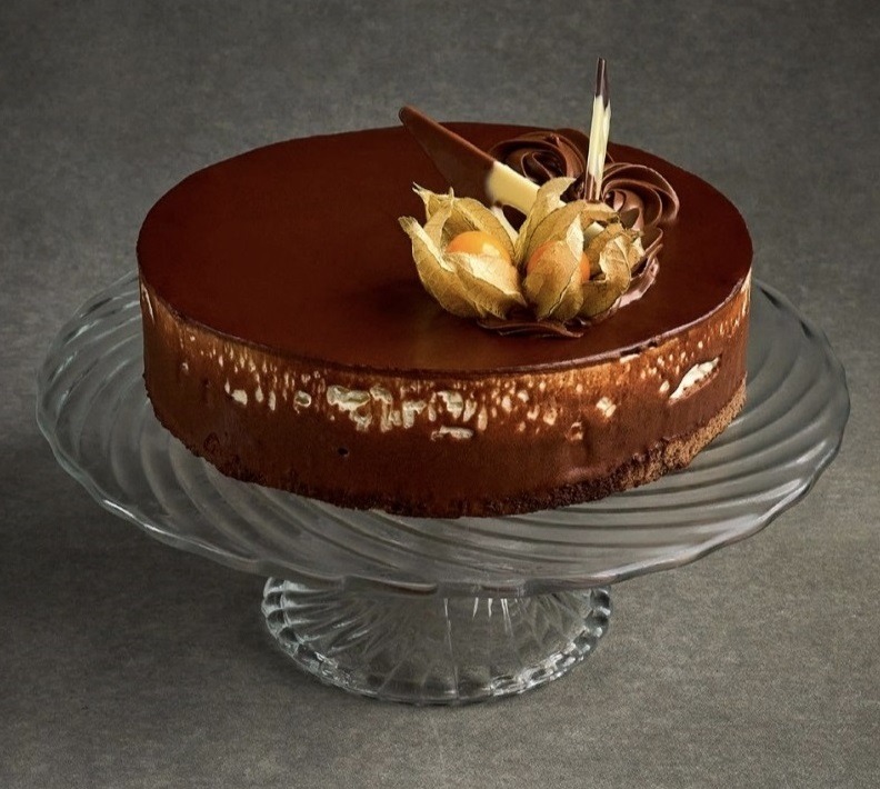 Elegancki tort czekoladowy na szklanej paterze z dekoracją z miechunki i czekoladowych ozdób. Gładka polewa i delikatne zdobienia tworzą wyrafinowany deser.