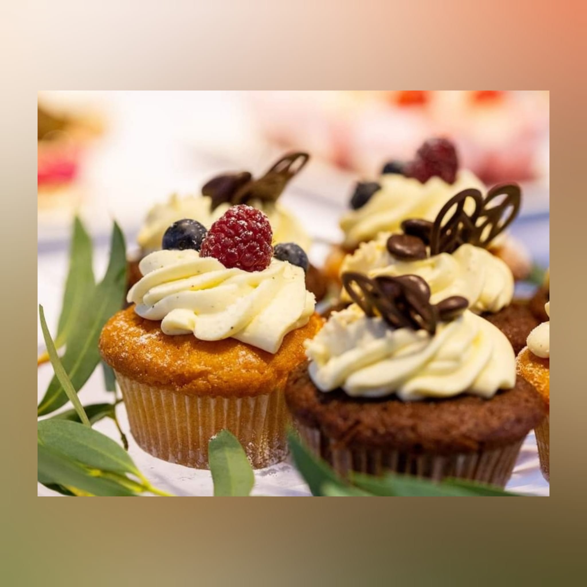 Dekoracyjne babeczki z kremem, malinami, borówkami i czekoladowymi ozdobami, ustawione na białym tle z zielonymi listkami. Słodki poczęstunek.