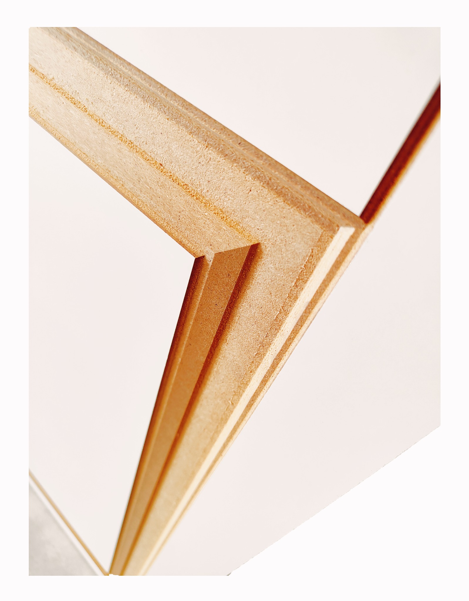 Precyzyjnie obrobiony, jasny element z płyty MDF z frezowanymi krawędziami pod kątem, widok z bliska na białym tle. Detal wykończeniowy.