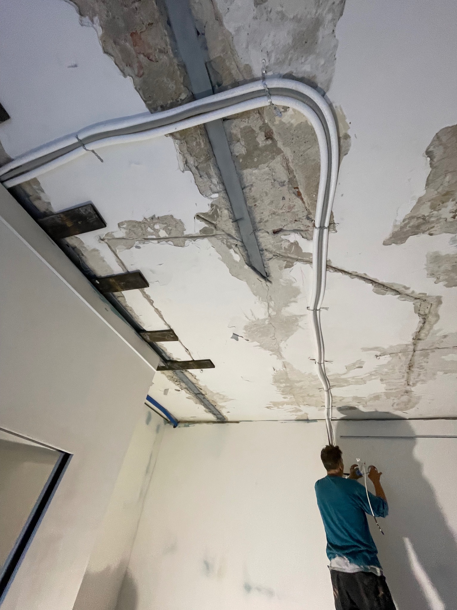 Montaż instalacji klimatyzacyjnej: białe rury prowadzone po suficie w surowym stanie, widoczny pracownik w trakcie pracy. Ujęcie z dołu, perspektywa wnętrza.