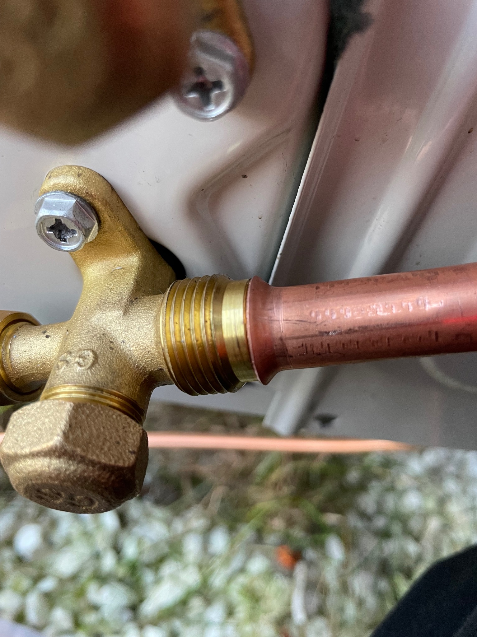 Mosiężny zawór z miedzianą rurką, element instalacji klimatyzacji, widoczne śruby mocujące i oznaczenia na rurce. Detal z bliska, instalacja wewnątrz budynku.