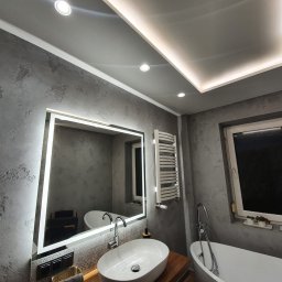 RemontLine - Szara łazienka z oświetleniem LED: lustro z ramą świetlną, grzejnik drabinkowy i owalna umywalka. Ściany w fakturze betonu, sufit z podświetleniem.