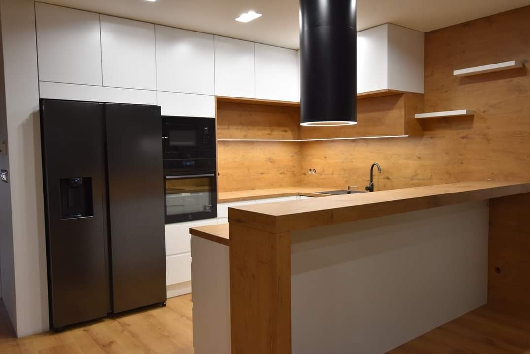 Nowoczesna kuchnia z białymi szafkami, drewnianym blatem i czarną lodówką side-by-side. Minimalistyczny design z oświetleniem LED pod szafkami.