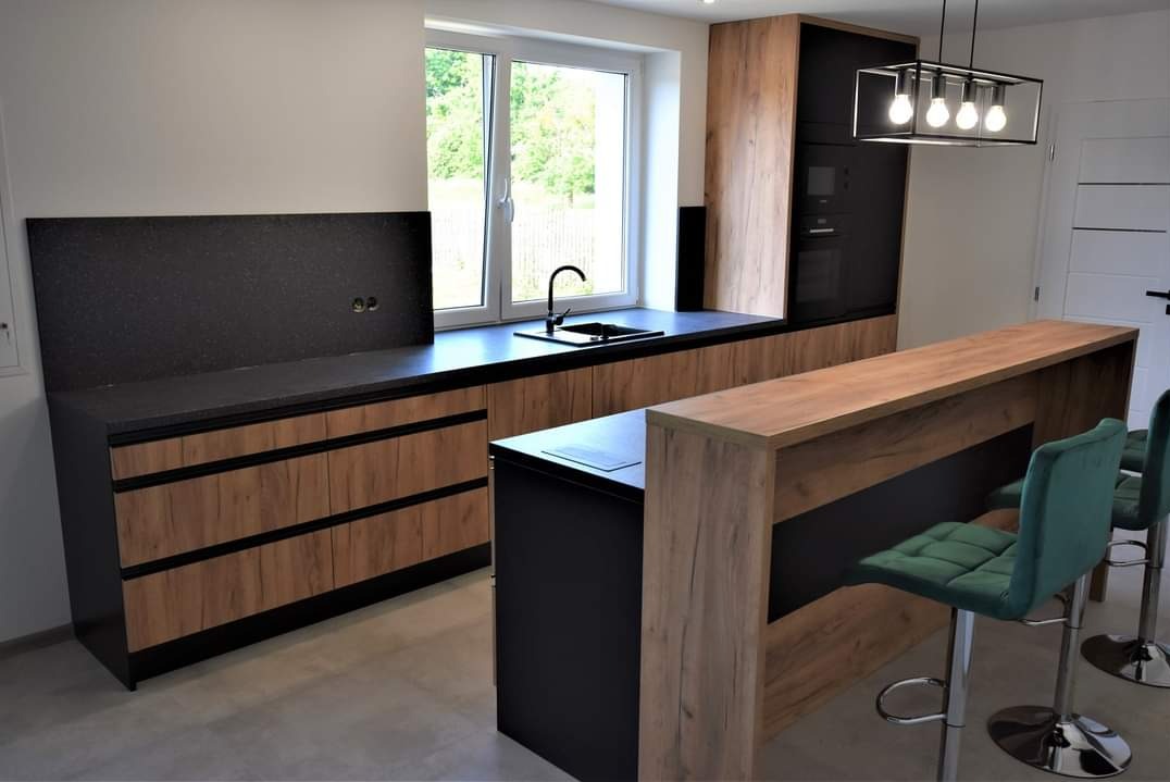 Nowoczesna kuchnia na wymiar z drewnianymi frontami, czarnym blatem i barkiem z zielonymi hokerami. Oświetlenie punktowe nad wyspą. Minimalistyczny design.