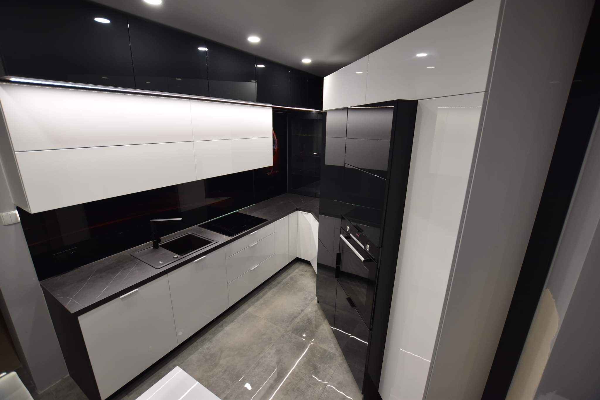 Nowoczesna kuchnia na wymiar w czerni i bieli, z połyskiem, Opole. Minimalistyczny design, czarne szkło na ścianie, szare płytki podłogowe. Eleganckie wykończenie.