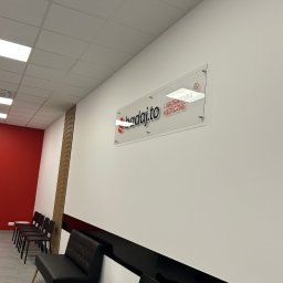 Magdalena Budzińska - Minimalistyczna poczekalnia laboratorium medycznego w Wilczynie. Białe ściany, czarne krzesła i sofa, logo na ścianie. Czyste i schludne wnętrze.