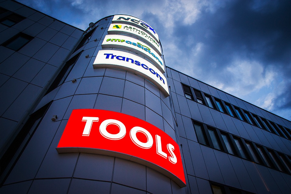 Elewacja budynku z podświetlanymi szyldami firm, widok z dołu, wieczorne niebo w tle. Szyld 'TOOLS' na pierwszym planie.