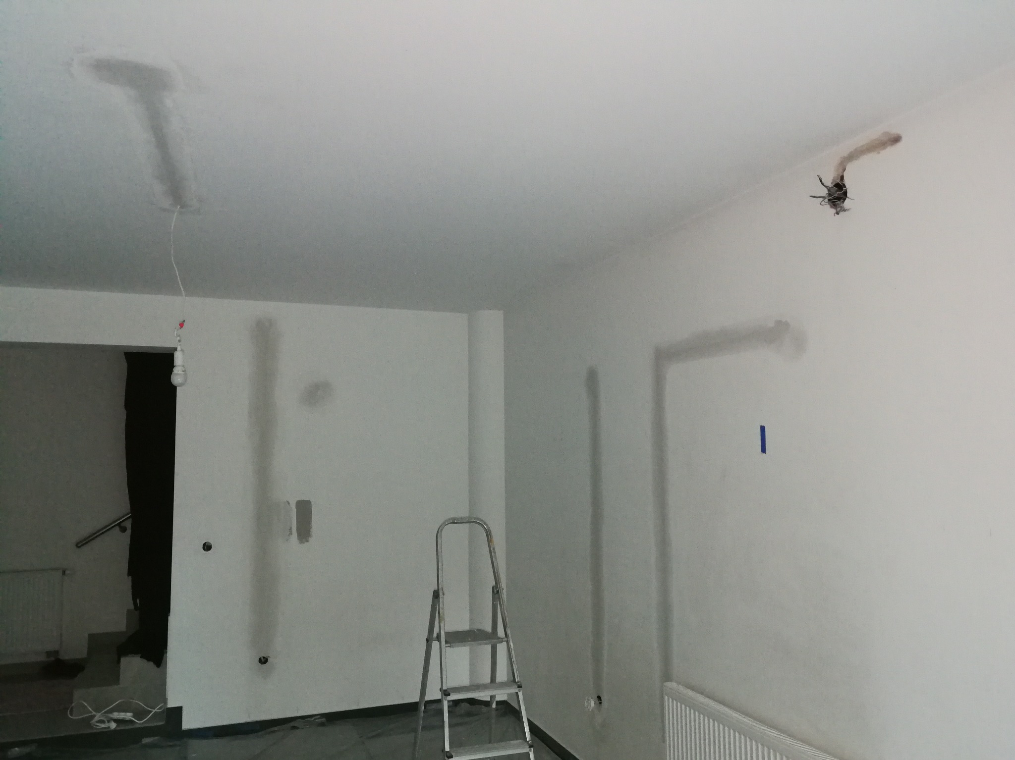 Świeżo wykończone wnętrze z widocznymi śladami po bruzdowaniu pod instalacje elektryczne, z przewodami wystającymi ze ściany i sufitu. Na podłodze folia ochronna.