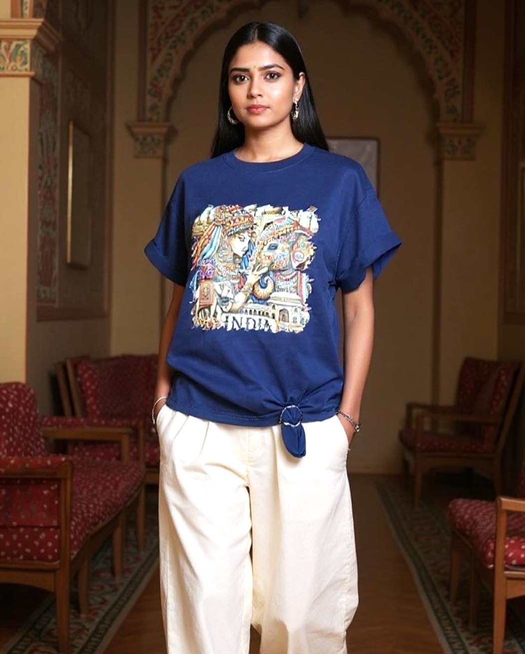 Kobieta prezentuje granatową koszulkę z indyjskim motywem graficznym i wiązaniem na dole, w eleganckim wnętrzu z krzesłami w tle.
