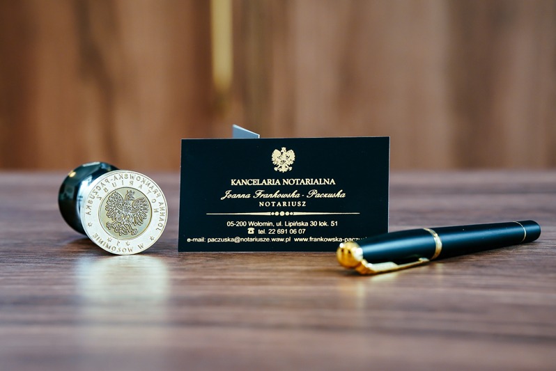 Wizytówka kancelarii notarialnej, pieczęć z godłem Polski i eleganckie pióro na drewnianym biurku. Detaliczne ujęcie, złote napisy, profesjonalizm.