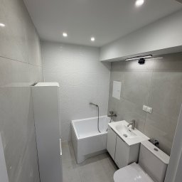 DAWID GRUSE DG USŁUGI - Nowoczesna łazienka w odcieniach szarości i bieli w Pile. Minimalistyczny design z wanną, umywalką z szafką i toaletą. Płytki z subtelnym wzorem.