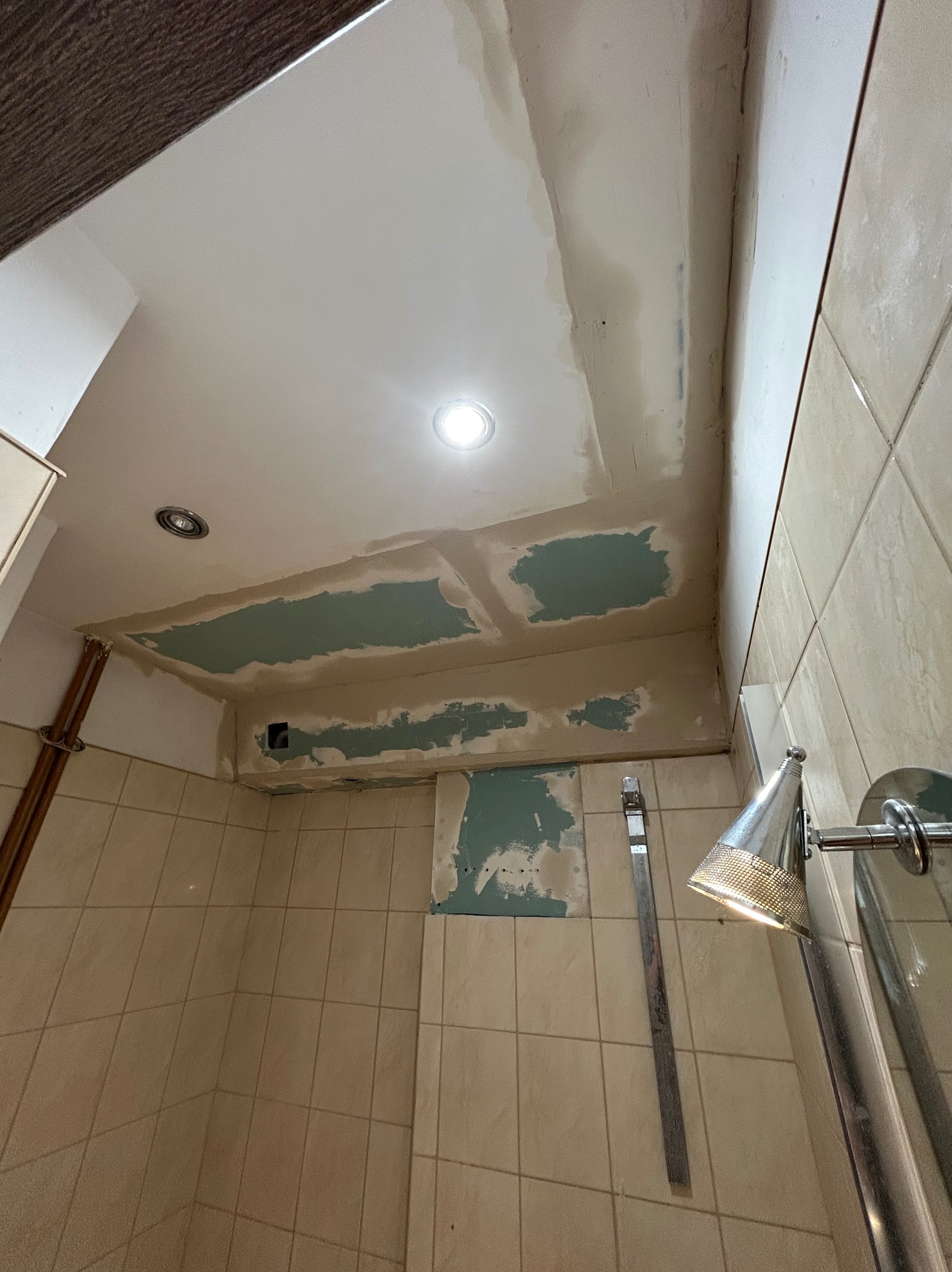 Nisko kątowe ujęcie łazienki w trakcie prac wykończeniowych. Widoczne fragmenty sufitu z nałożoną gładzią, fragment ściany z płytkami i element armatury.