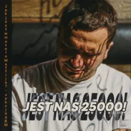 Mężczyzna w koszulce z napisem 'JEST NAS 25000!' w miejskim otoczeniu, oświetlony światłem słonecznym.