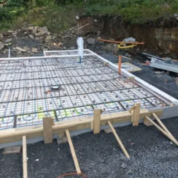 Przygotowanie fundamentu pod dom szkieletowy: zbrojenie, instalacja ogrzewania podłogowego, szalunek drewniany. Widok z góry, teren budowy.