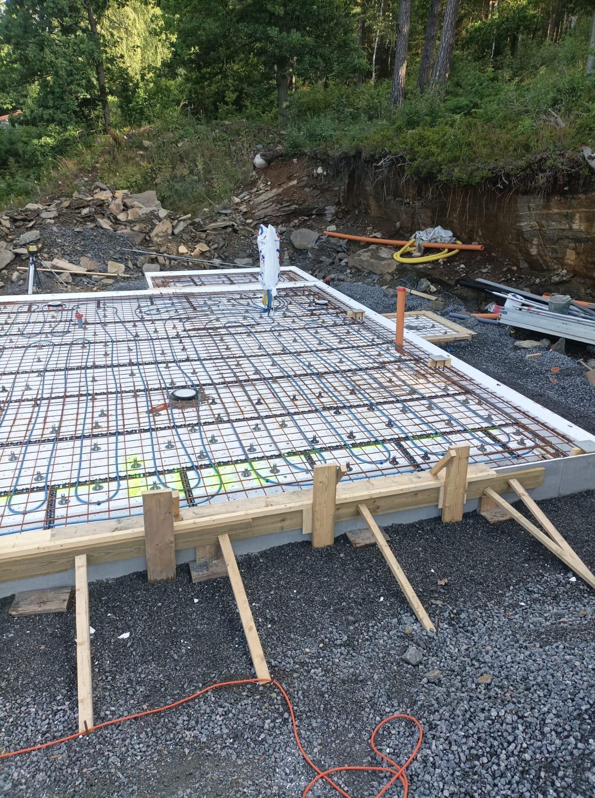 Przygotowanie fundamentu pod dom szkieletowy: zbrojenie, instalacja ogrzewania podłogowego, szalunek drewniany. Widok z góry, teren budowy.