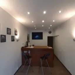 Wnętrze biura IT z recepcją, dwoma krzesłami barowymi, oświetleniem punktowym i dekoracjami ściennymi. Na ścianie wisi monitor.