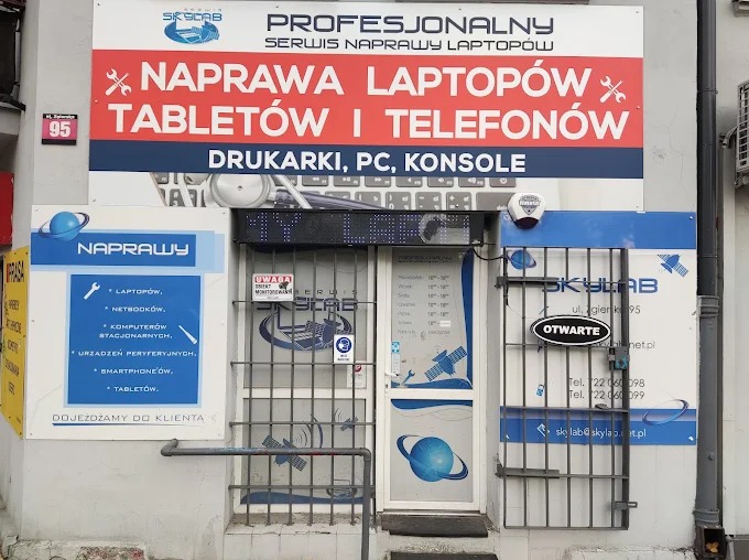Fasada serwisu SkyLab z szyldem 'Naprawa laptopów, tabletów i telefonów'. Widoczne godziny otwarcia i adres. Logo firmy z motywem planety.