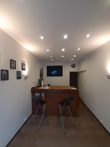 Wnętrze biura IT z recepcją, dwoma krzesłami barowymi, oświetleniem punktowym i dekoracjami ściennymi. Na ścianie wisi monitor.