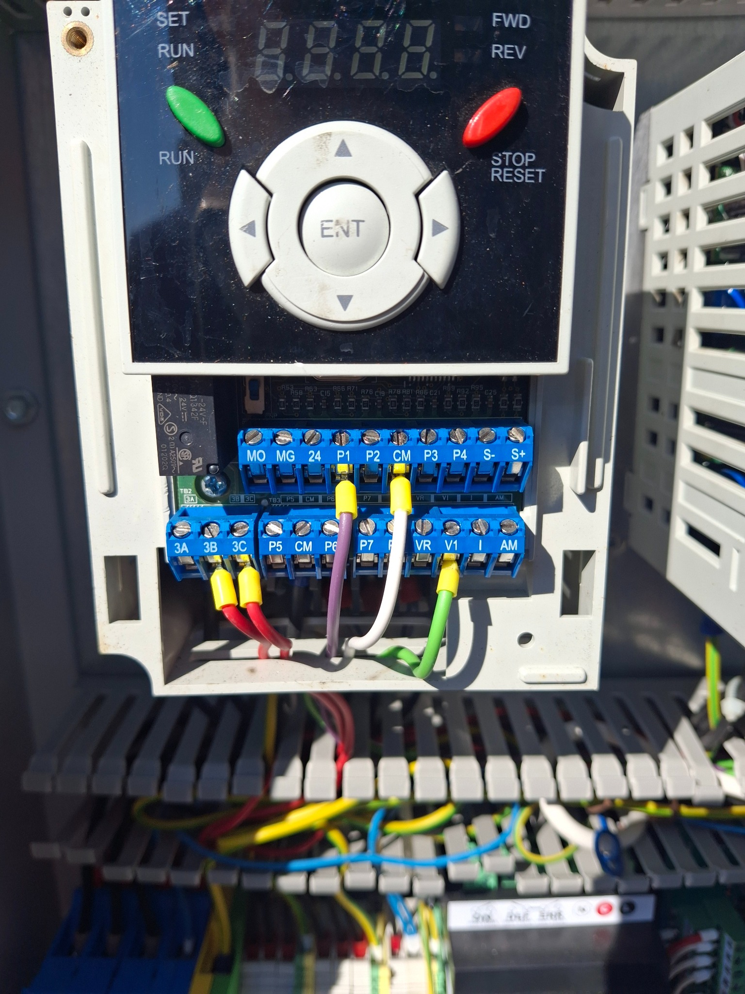 Panel sterowania z podłączonymi kablami, widoczne złącza i oznaczenia. Instalacja elektryczna w szarej obudowie, kable w różnych kolorach.